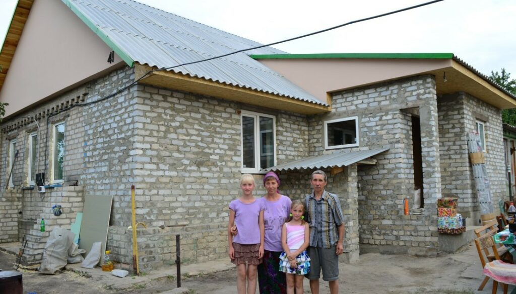Bombed family in front of rebuilt house